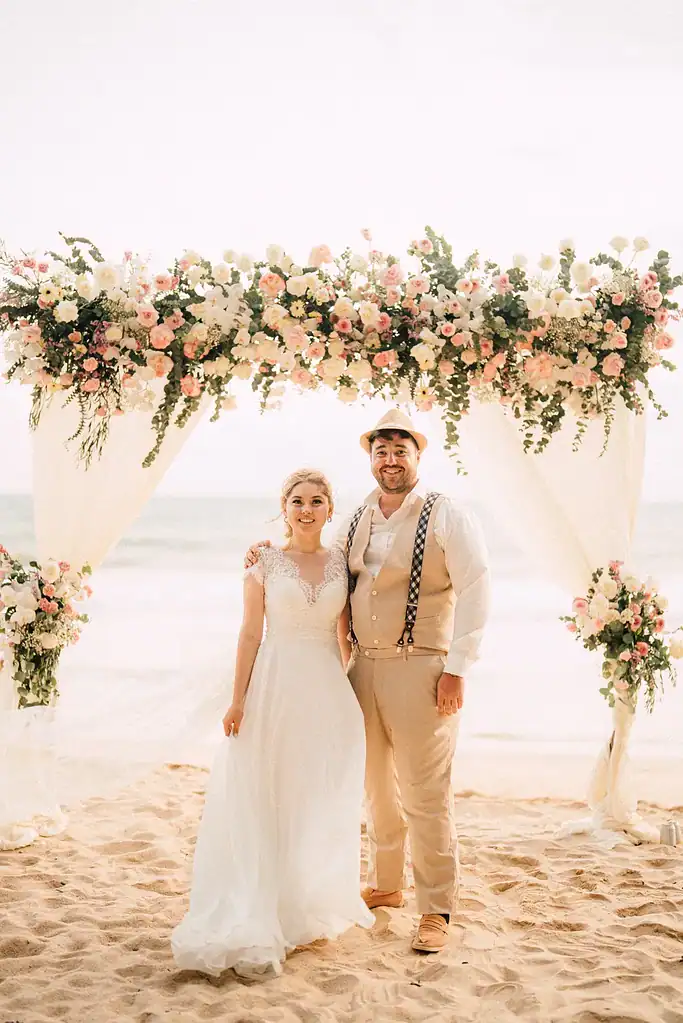 Jaen and Leila under a floral ceremony arch on Layan Beach, Phuket, during their private beach elopement
