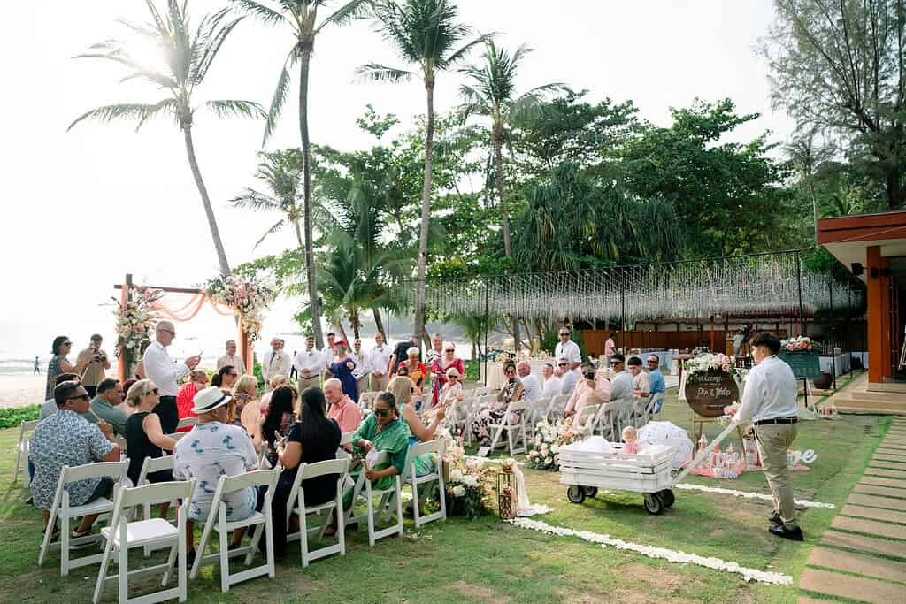 A resort wedding ceremony on Phuket with guests seated under a floral arch overlooking the sea.